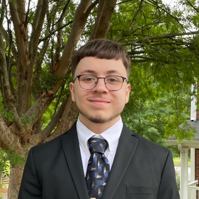 Headshot of Diego Gonzalez Alicata wearing a dark suit and glasses, outdoors