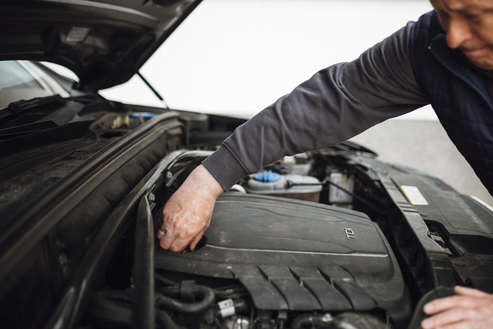 A mechanic leans over an open car hood, inspecting the engine during a pre-purchase or maintenance check